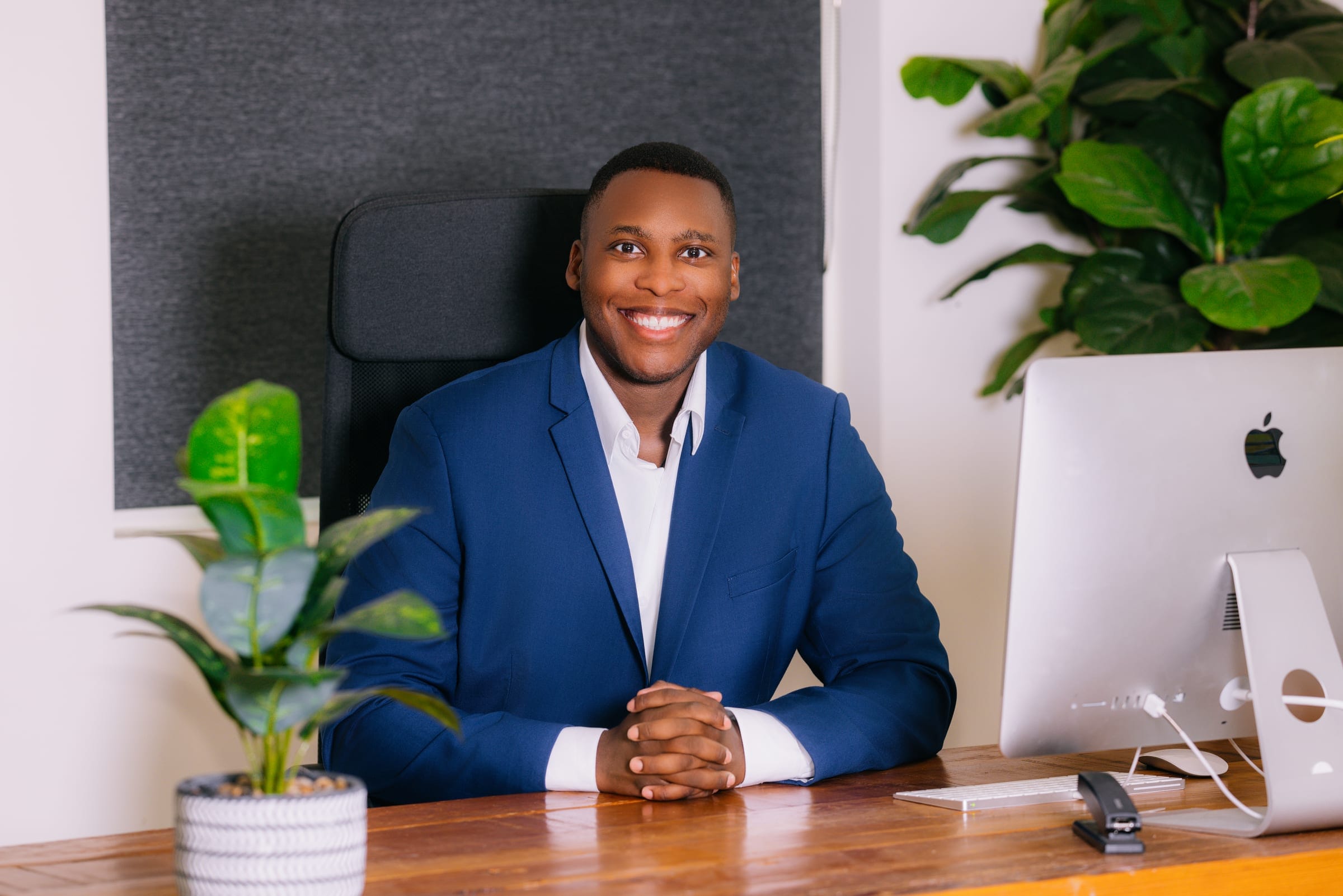 Lyndon Hector smiling at his desk in a navy blazer